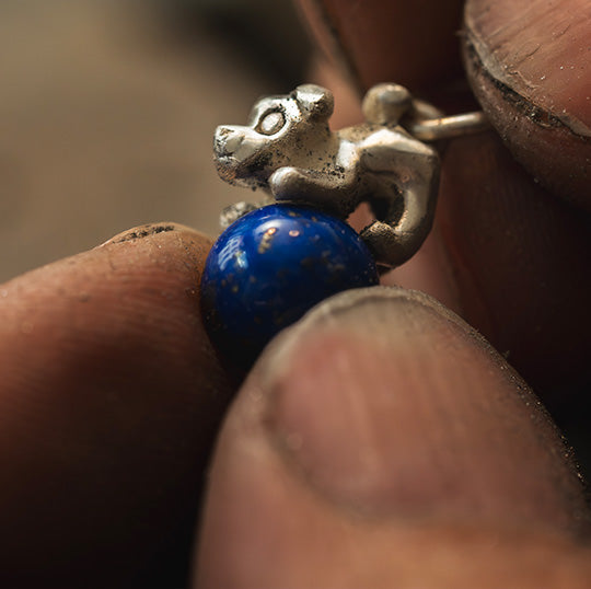 jewellery charm of a dog figurine on a ball of lapis lazuli, in the making, showcasing intricate details and vibrant colors in a captivating display of craftsmanship